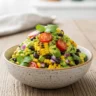 Close up bowl of chunky corn black bean guacamole with cilantro and lime
